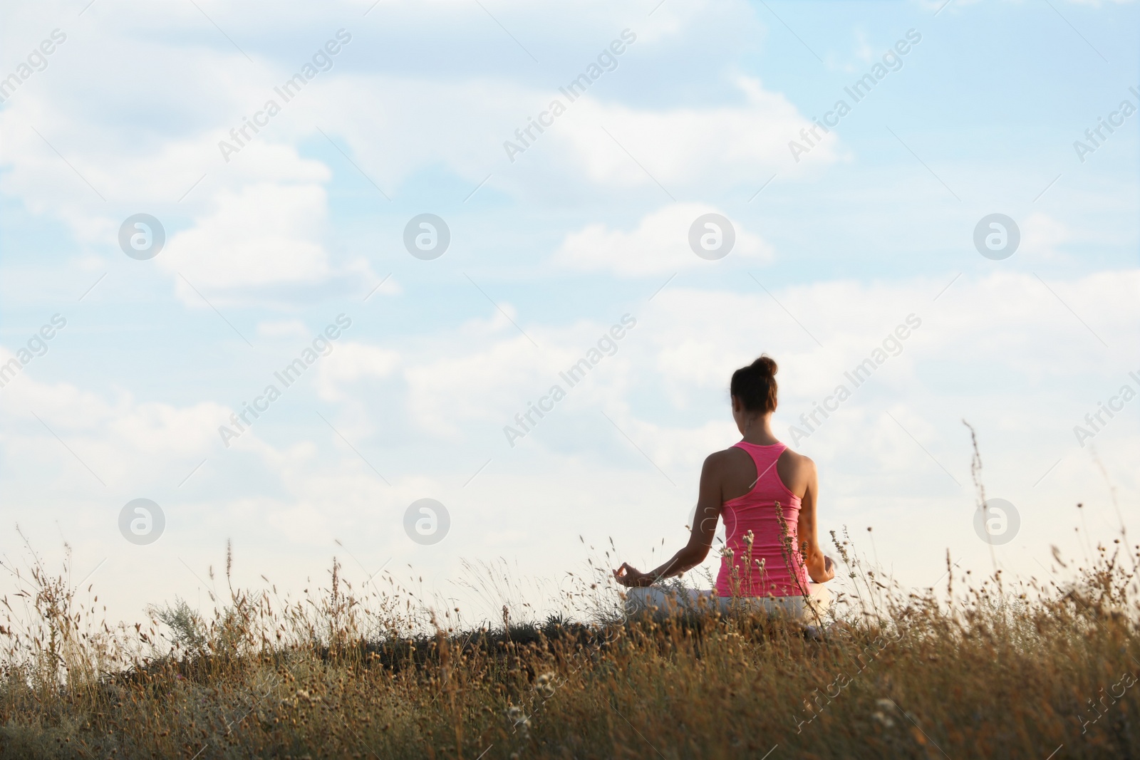 Photo of Woman meditating in meadow, back view. Space for text