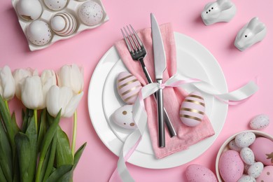 Photo of Festive table setting with painted eggs and tulips on pink background, flat lay. Easter celebration