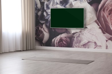 Image of Modern wide screen TV on wall in room with yoga mat