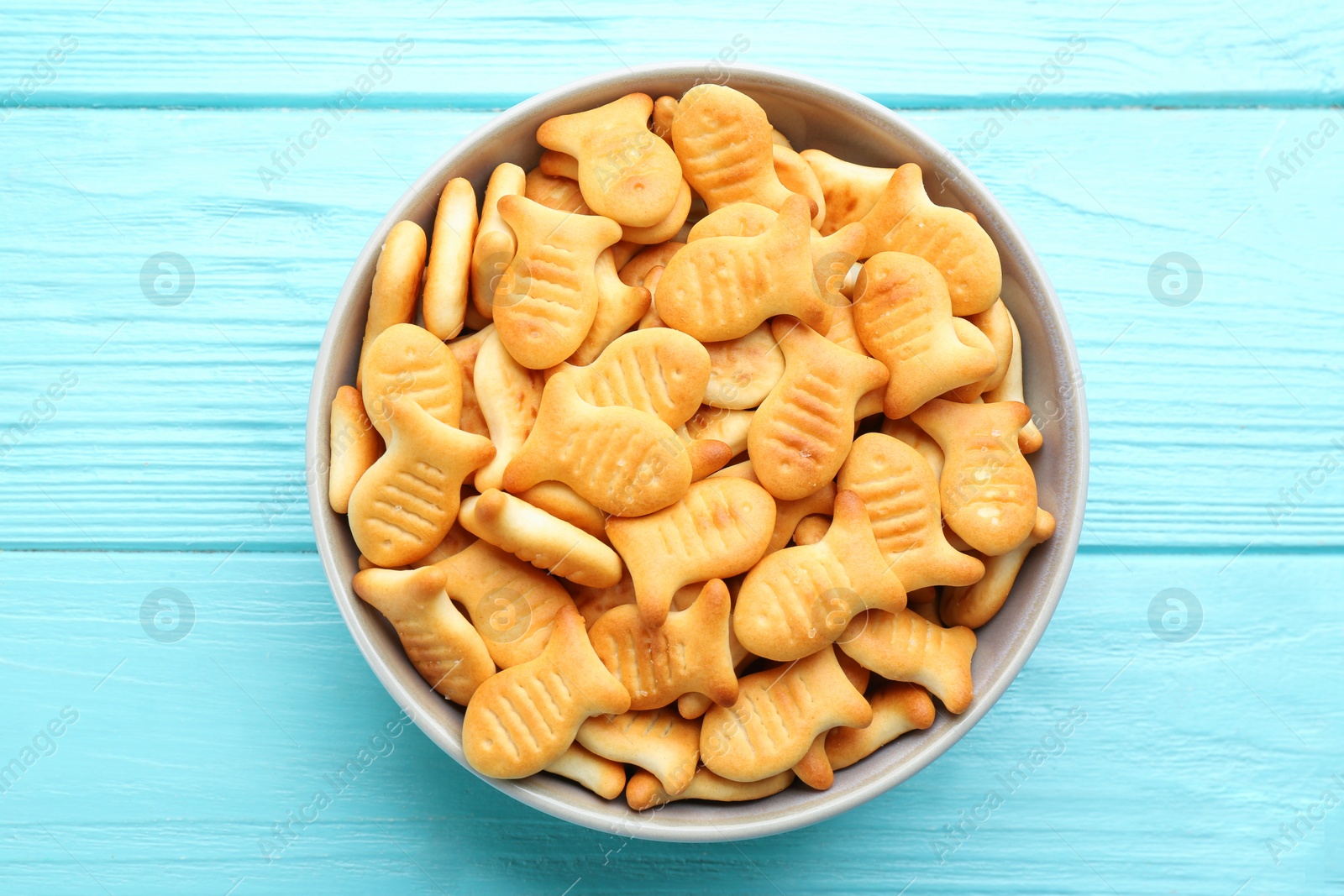 Photo of Delicious goldfish crackers in bowl on light blue wooden table, top view