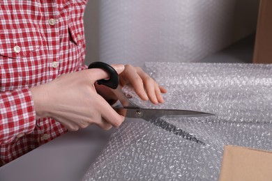 Photo of Woman cutting bubble wrap at table in warehouse, closeup