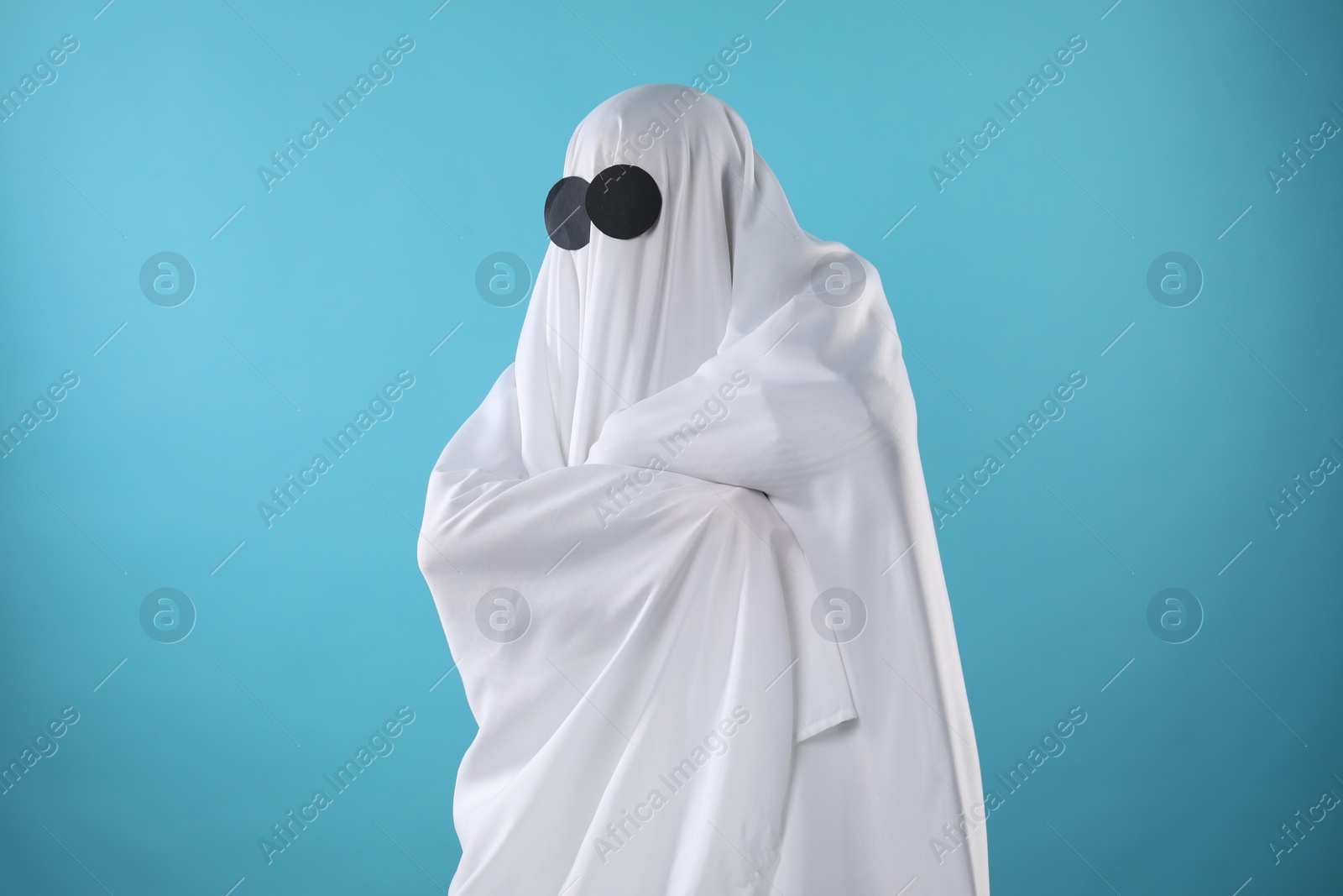 Photo of Creepy ghost. Person covered with white sheet on light blue background