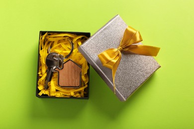 Photo of Key with trinket in shape of house and gift box on light green background, flat lay. Housewarming party