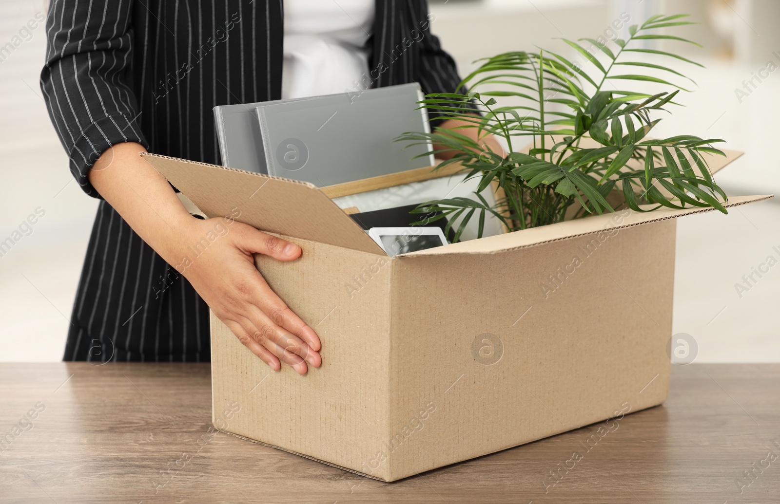 Photo of Unemployment problem. Woman with box of personal belongings at table in office, closeup
