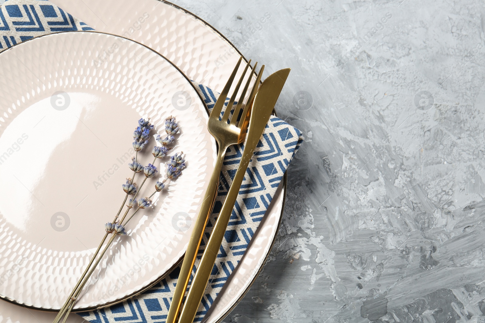Photo of Clean plates, cutlery, napkin and lavender flowers on light grey textured table, above view. Space for text