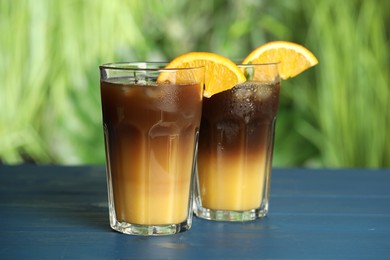 Photo of Tasty refreshing drink with coffee and orange juice on blue wooden table against blurred background
