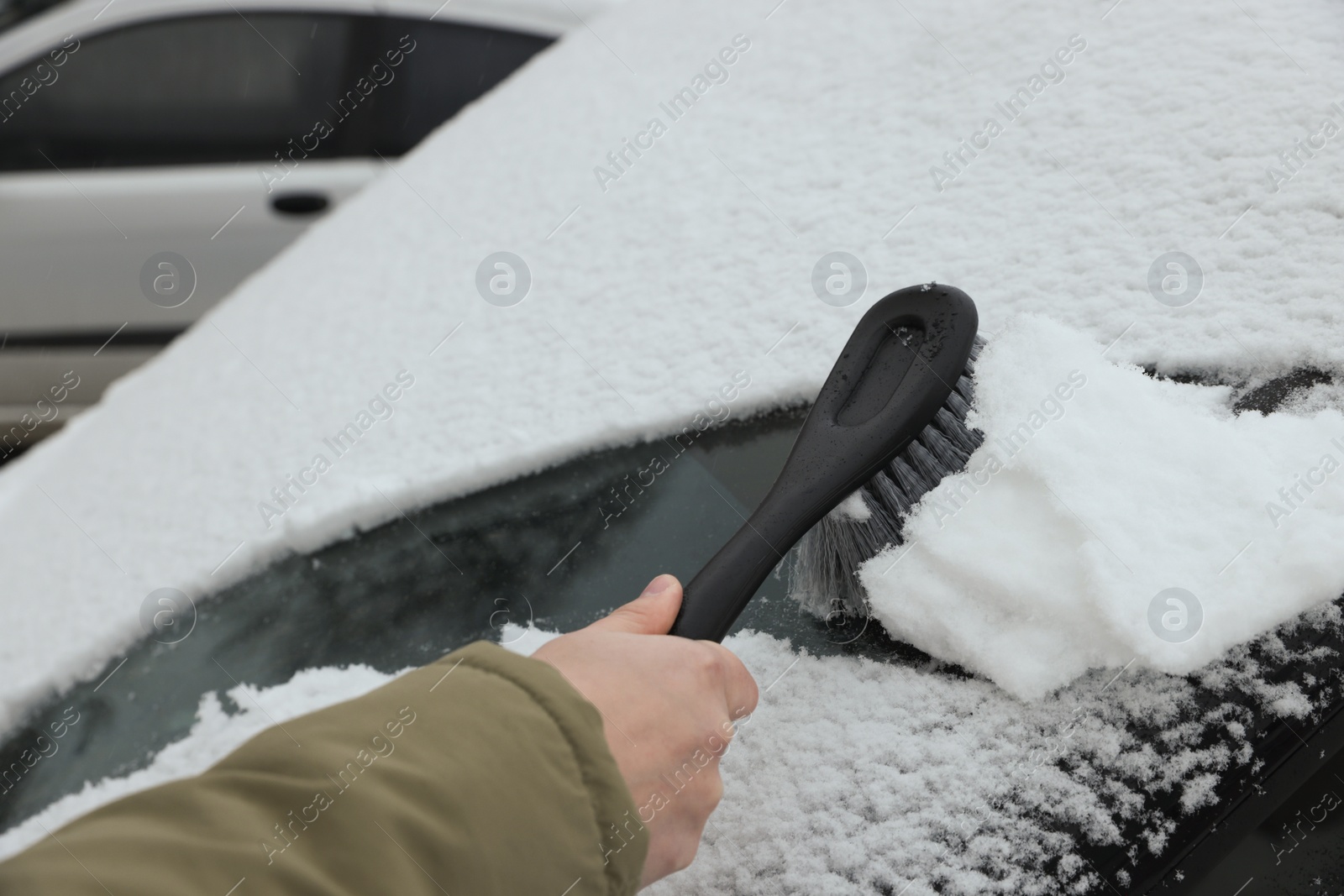 Photo of Woman cleaning car windshield from snow with brush outdoors, closeup