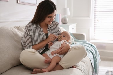 Happy mother holding her cute little baby with pacifier at home