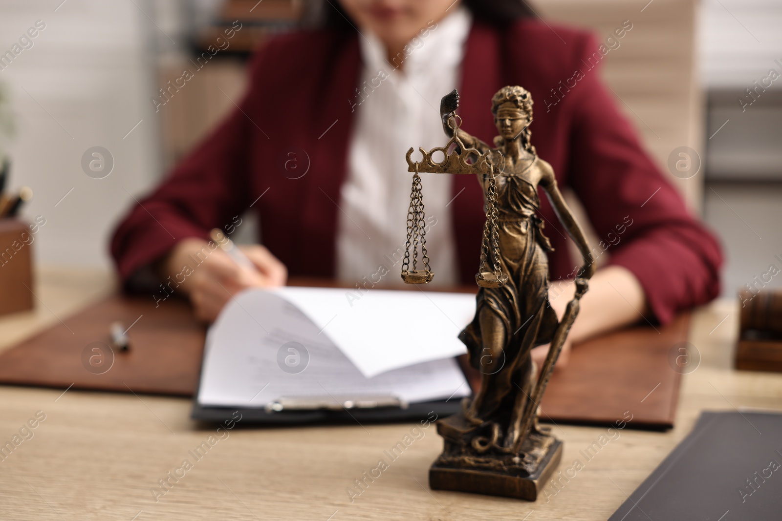 Photo of Notary signing document at table in office, focus on statue of Lady Justice