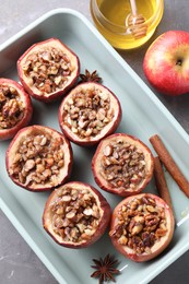 Tasty baked apples with nuts, honey and spices in dish on gray table, flat lay