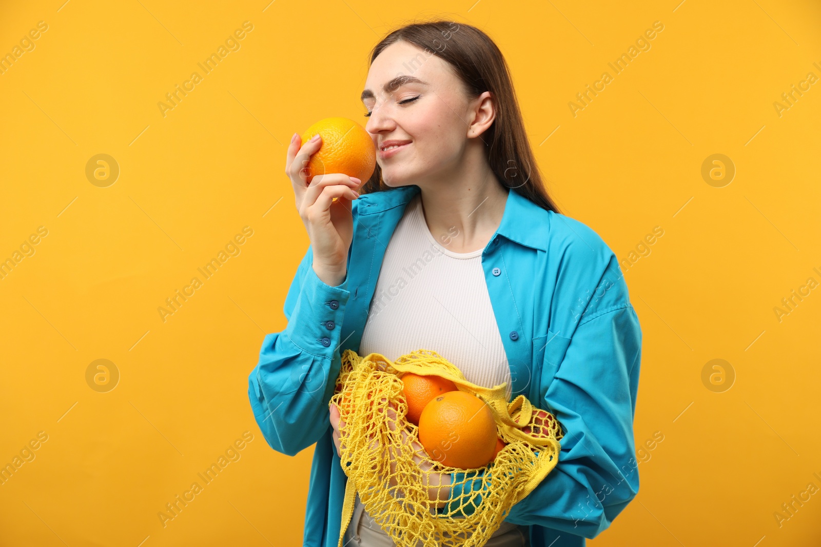 Photo of Woman with string bag of fresh oranges on orange background