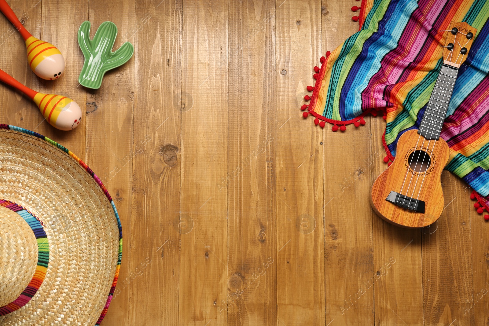 Photo of Mexican sombrero hat, maracas, toy cactus, guitar and colorful poncho on wooden background, flat lay. Space for text