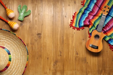 Mexican sombrero hat, maracas, toy cactus, guitar and colorful poncho on wooden background, flat lay. Space for text