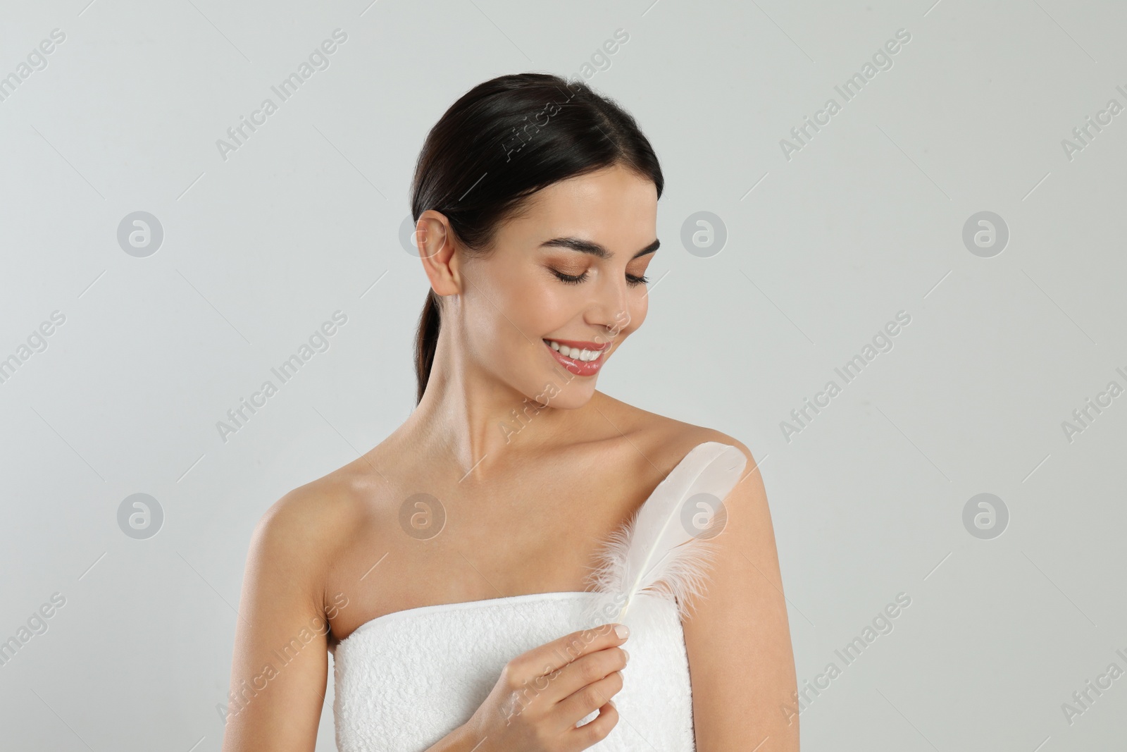 Photo of Young woman with feather on light grey background. Epilation concept