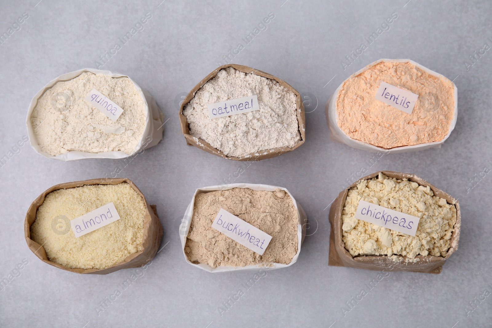 Photo of Sacks with different types of flours on light grey table, flat lay