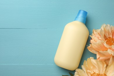 Photo of Bottle of fabric softener and beautiful peony flowers on light blue wooden table, flat lay. Space for text