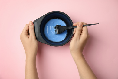 Photo of Woman preparing dye for hair coloring on pink background, top view