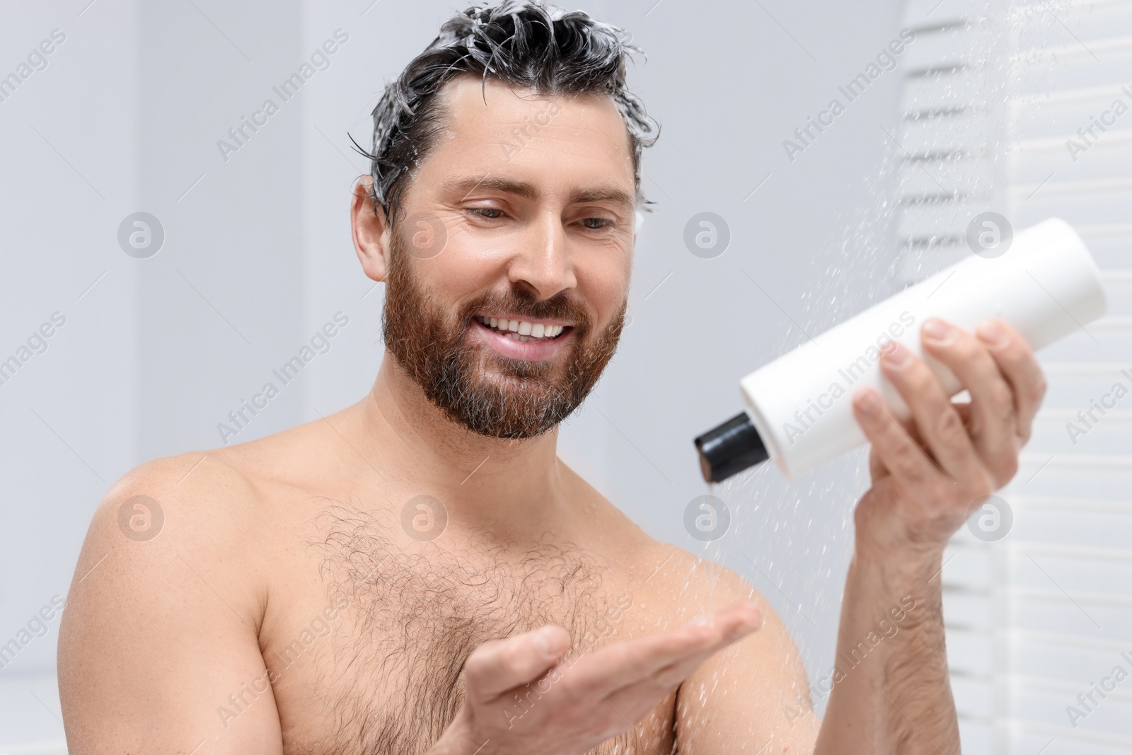 Photo of Happy man pouring shampoo onto his hand in shower