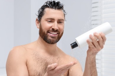 Happy man pouring shampoo onto his hand in shower