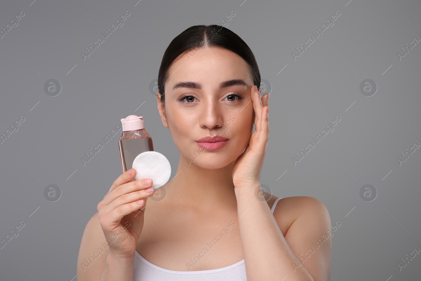 Photo of Beautiful woman with makeup remover and cotton pad on gray background