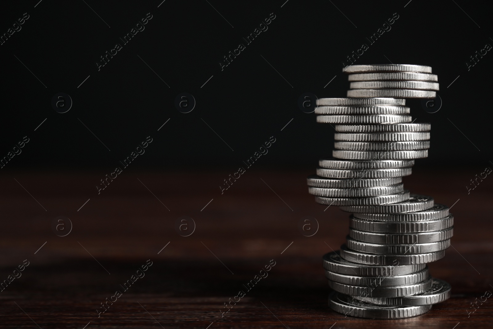 Photo of Many coins stacked on wooden table against black background, space for text