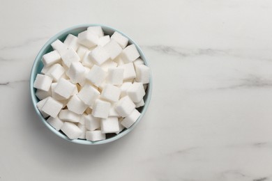 Photo of Bowl of white sugar cubes on marble table, top view. Space for text
