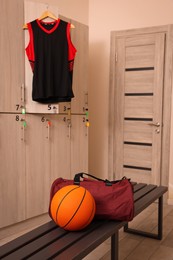 Photo of Sports bag and basketball ball on wooden bench in locker room