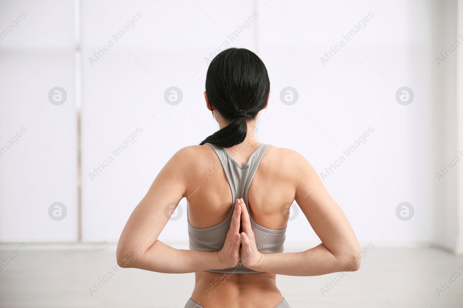 Photo of Young woman practicing seiza asana in yoga studio, back view. Vajrasana pose