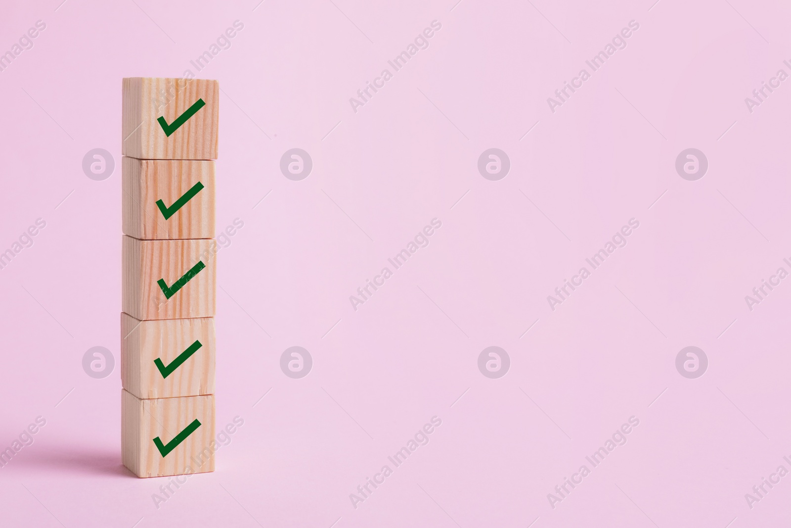Image of Stacked wooden cubes with check marks on pale pink background. Space for text