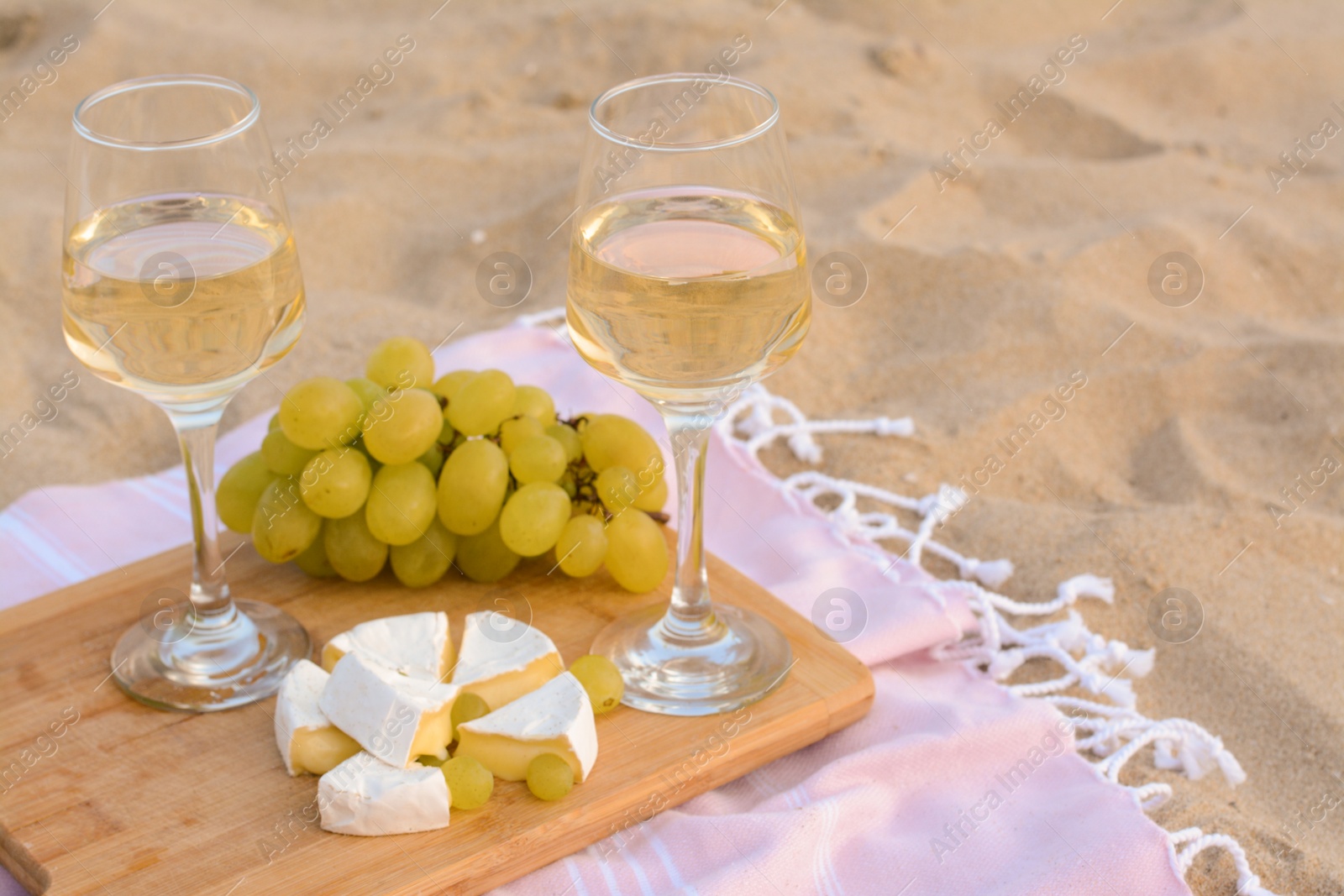 Photo of Glasses with white wine and snacks for beach picnic on sand outdoors