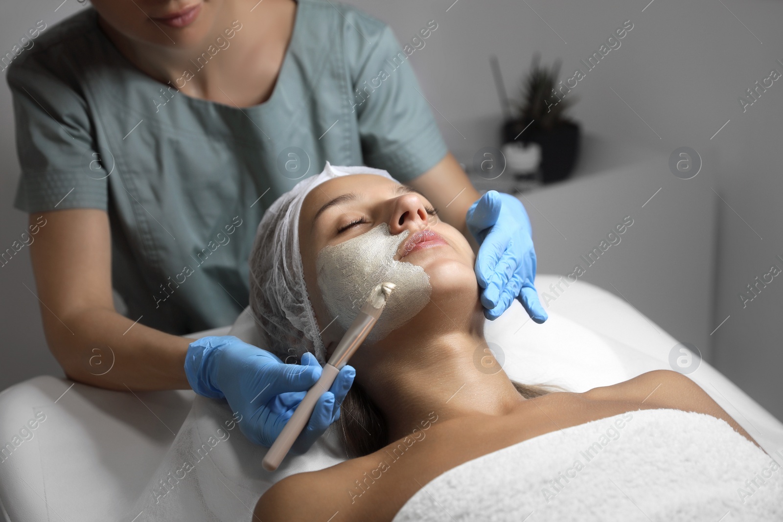 Photo of Cosmetologist applying mask on client's face in spa salon