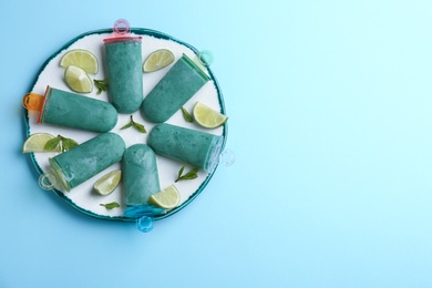 Photo of Plate with spirulina popsicles, mint and lime slices on color background, top view. Space for text