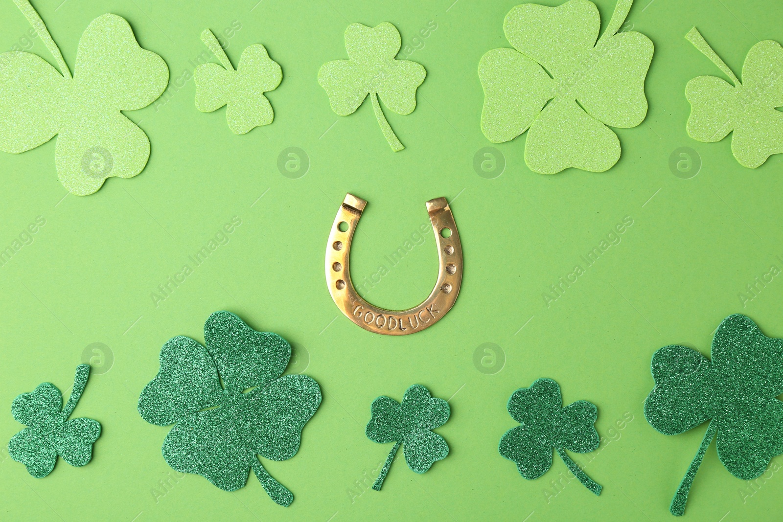 Photo of St. Patrick's day. Golden horseshoe and decorative clover leaves on green background, flat lay