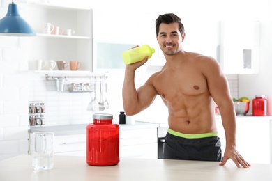 Young shirtless athletic man with protein shake powder in kitchen, space for text