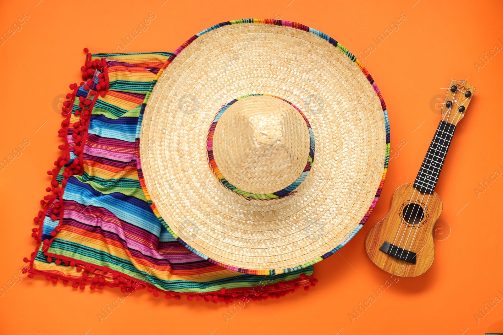 Photo of Mexican sombrero hat, guitar and colorful poncho on orange background, flat lay