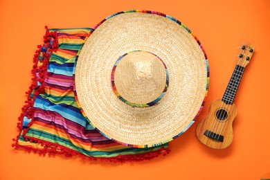 Photo of Mexican sombrero hat, guitar and colorful poncho on orange background, flat lay