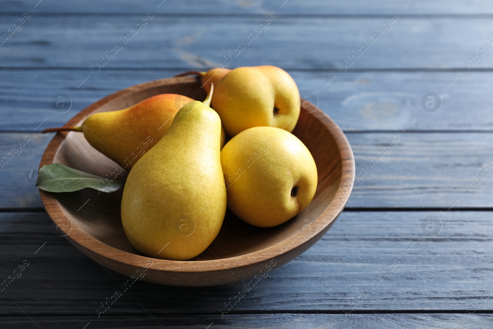 Photo of Plate with ripe pears on blue wooden background. Space for text