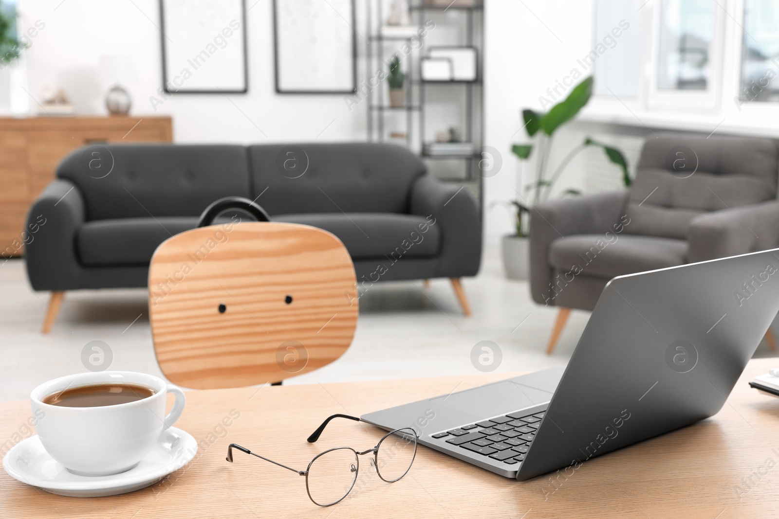 Photo of Home workspace. Laptop, glasses and cup of coffee on wooden desk in room