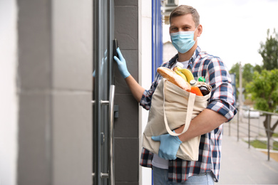 Photo of Male volunteer with products ringing doorbell outdoors. Aid during coronavirus quarantine