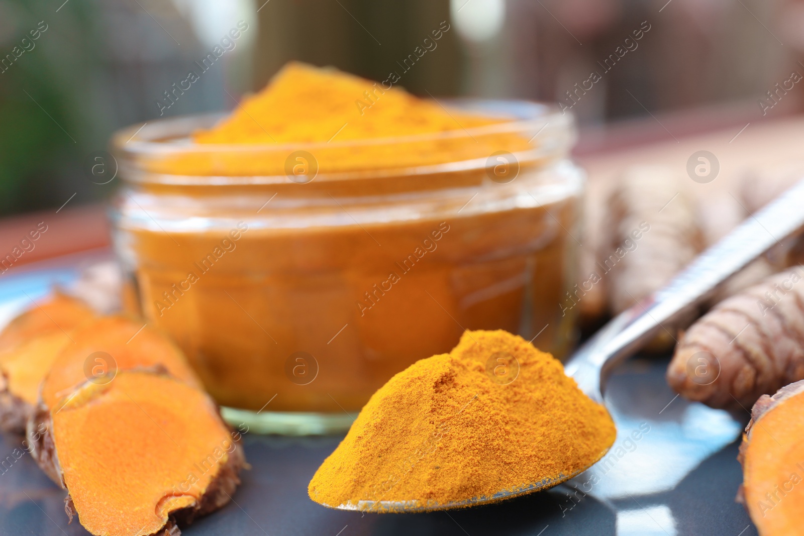 Photo of Plate with glass jar of turmeric powder and fresh roots on table, closeup