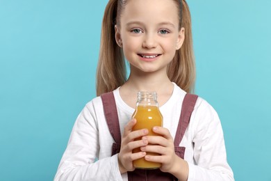 Cute little girl holding glass bottle of fresh juice on light blue background