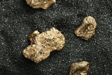 Photo of Shiny gold nuggets on black sand, top view