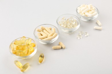 Photo of Glass bowls with different vitamin capsules on light grey background