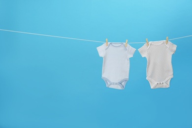 Colorful baby onesies hanging on clothes line against blue background, space for text. Laundry day