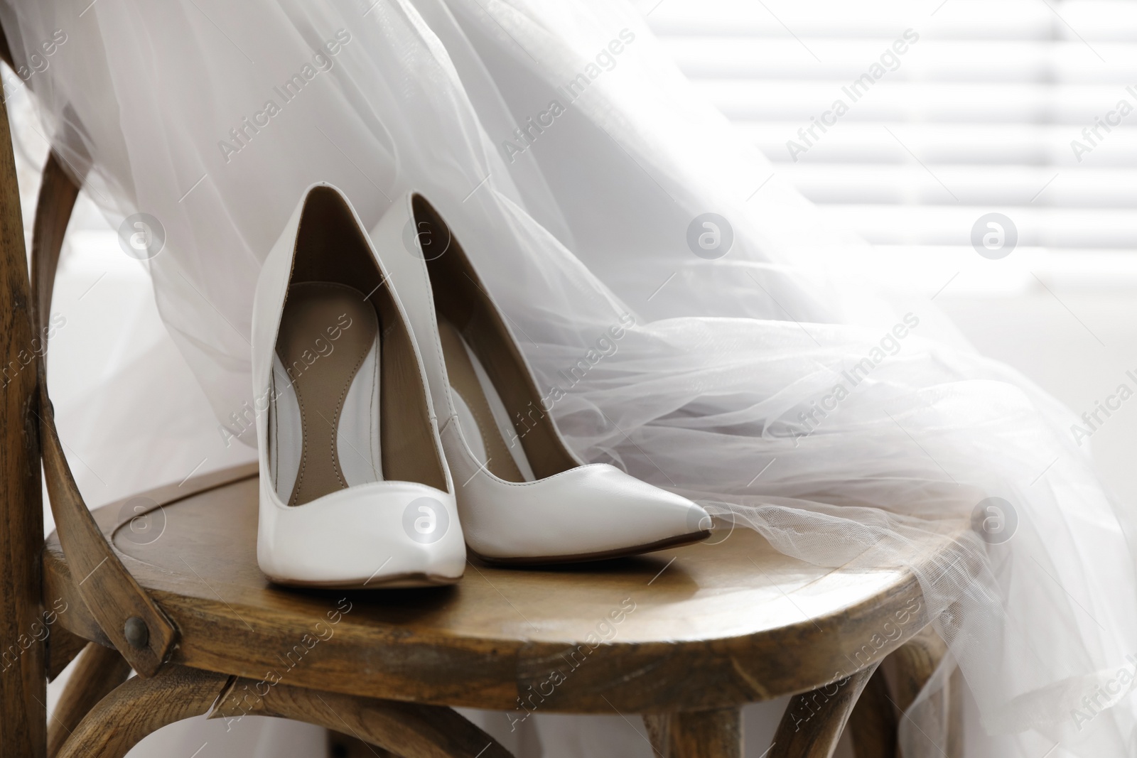 Photo of Pair of white wedding high heel shoes and veil on wooden chair indoors