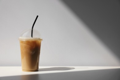 Photo of Plastic takeaway cupdelicious iced coffee on white table under sunlight, space for text