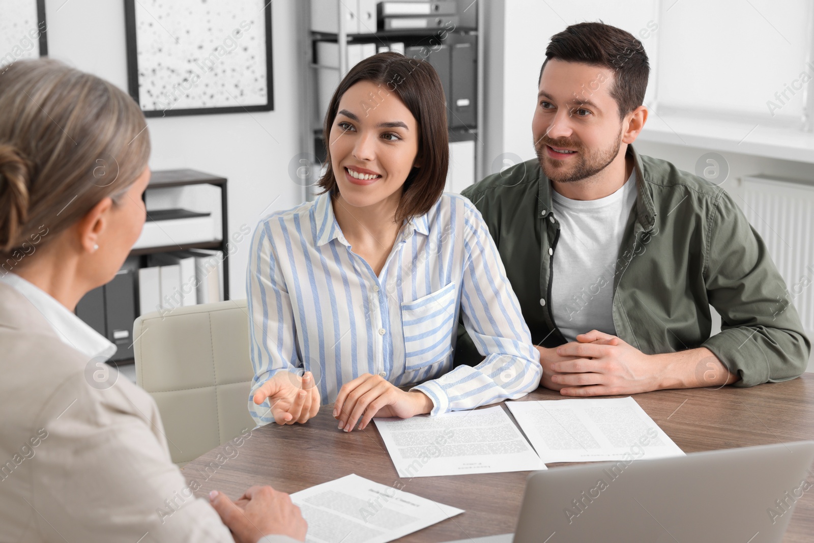 Photo of Young couple consulting insurance agent about pension plan at wooden table indoors