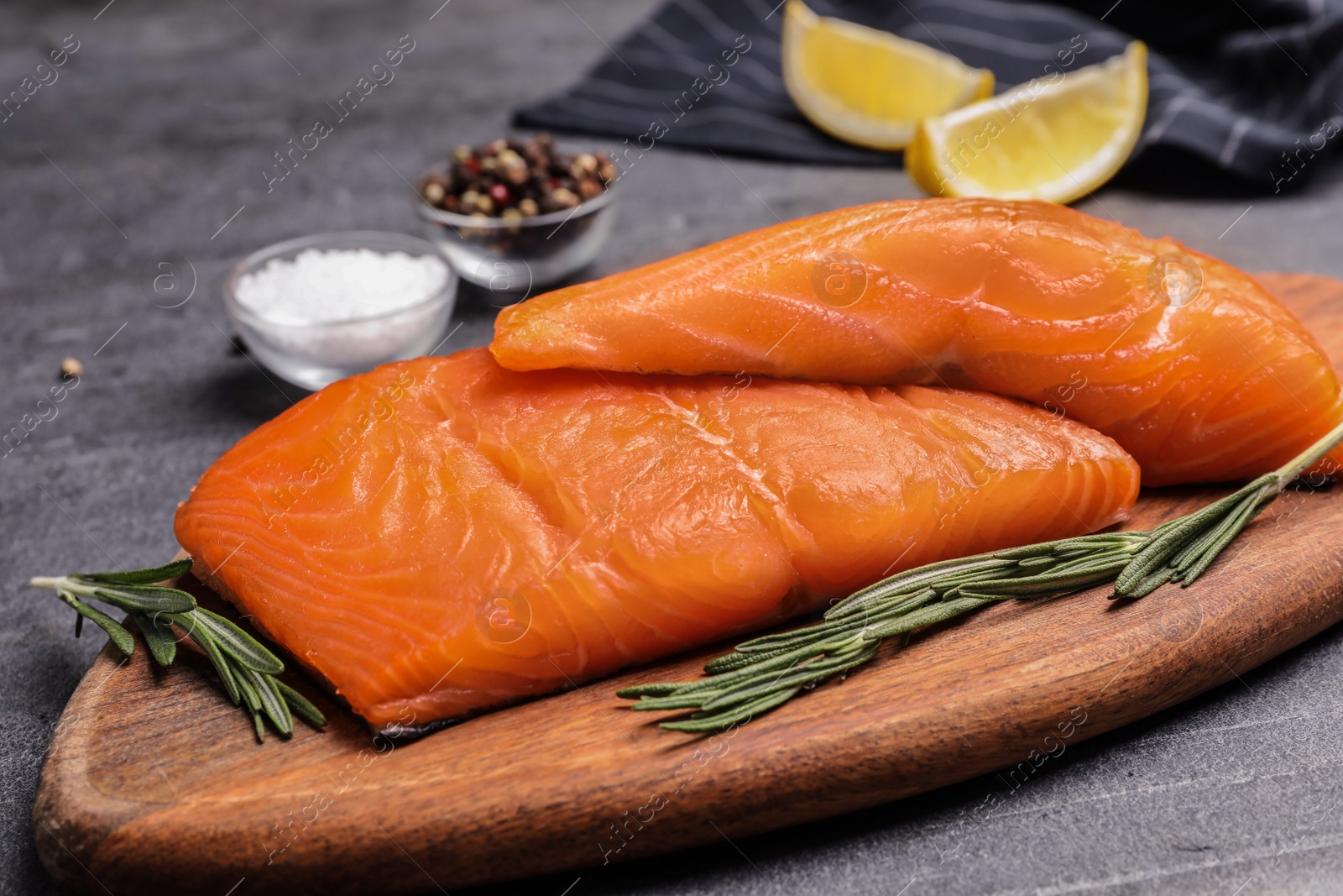 Photo of Wooden board with salmon fillet on grey table, closeup