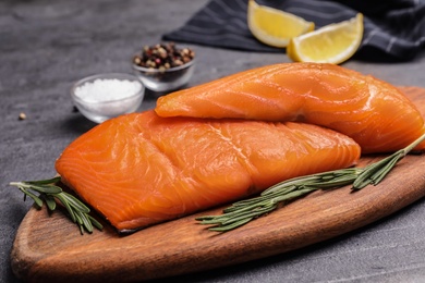 Wooden board with salmon fillet on grey table, closeup
