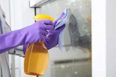 Photo of Woman cleaning window with rag and detergent indoors, closeup